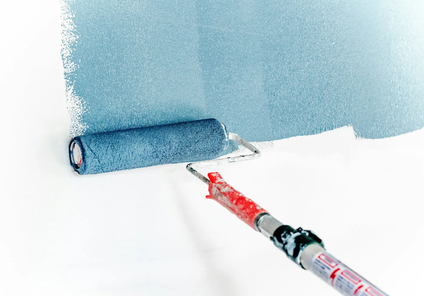 Rullo che stende pittura blu su una parete bianca